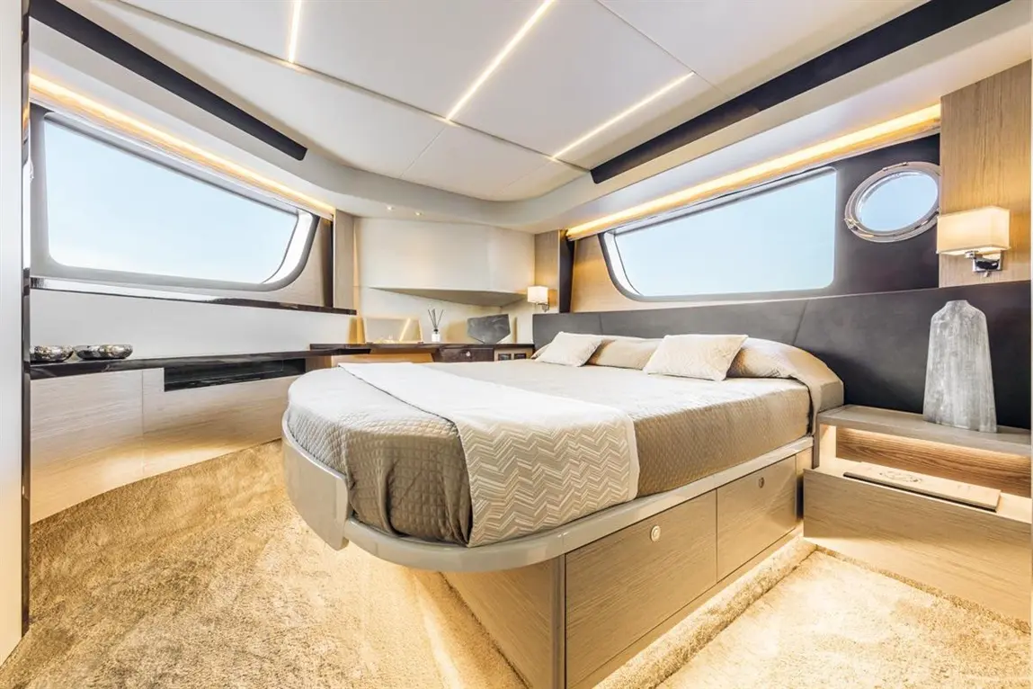 Modern bedroom with a large bed, sleek furnishings, and ample natural light from curved windows. Soft neutral tones throughout.